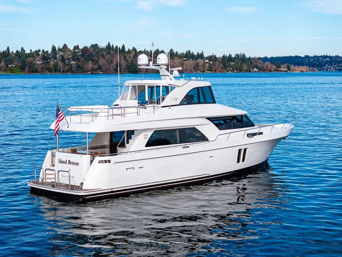 A sleek white yacht cruises gracefully on calm waters with a scenic shoreline in the background. aboard ISLAND BREEZE Yacht for Sale