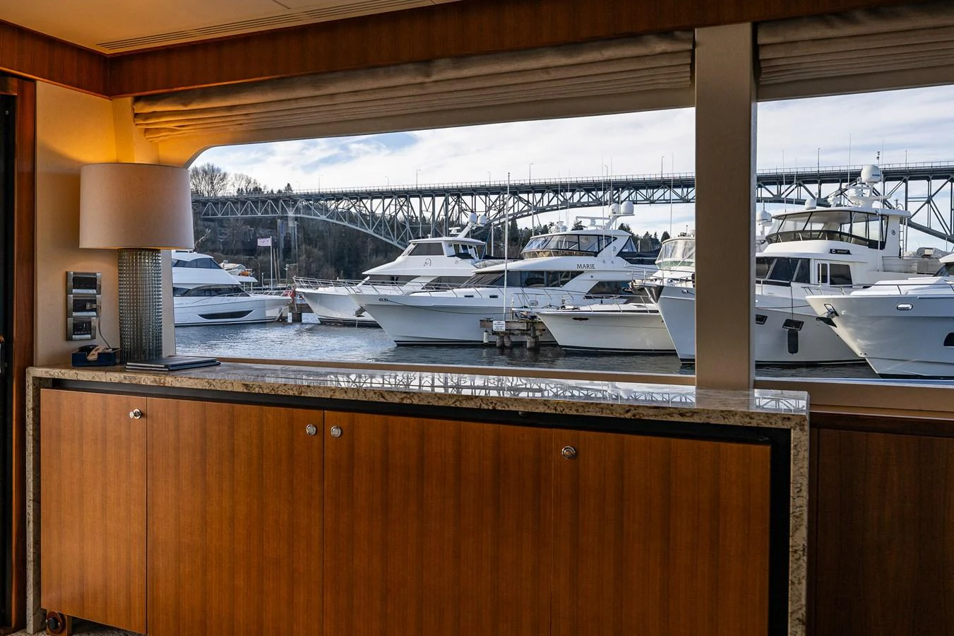 The image captures a serene view from the yacht's interior, showcasing a wooden cabinet and a large window overlooking a marina with several yachts docked. aboard ISLAND BREEZE Yacht for Sale
