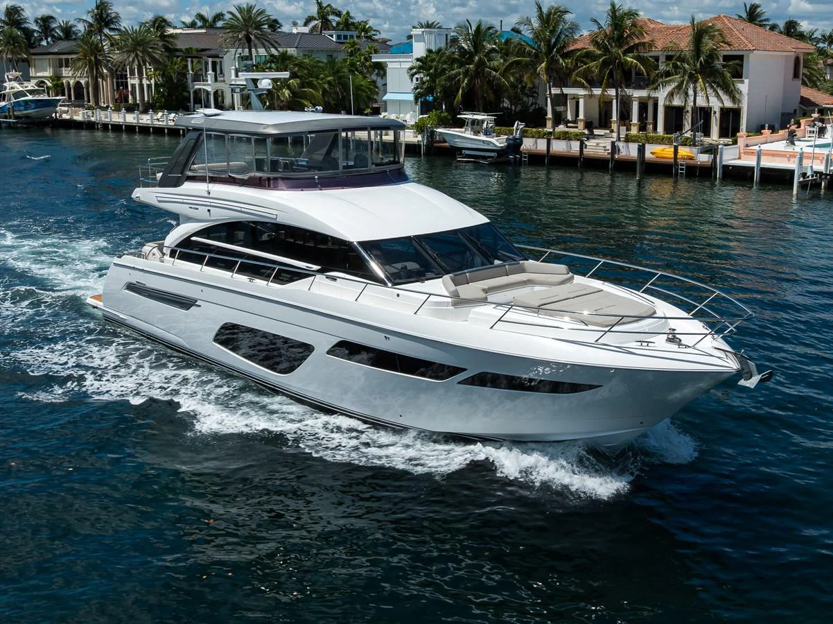 A sleek, modern yacht cruising through a serene waterway with luxurious waterfront homes in the background. aboard MISS AMY Yacht for Sale