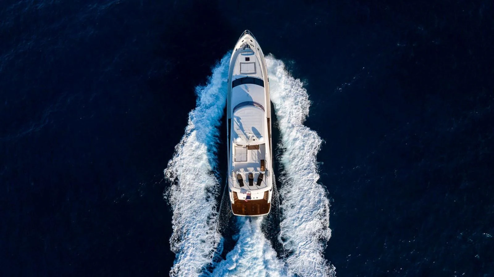 Aerial view of a luxurious yacht cruising through deep blue waters, leaving a trail of white wake. aboard OASIS Yacht for Sale