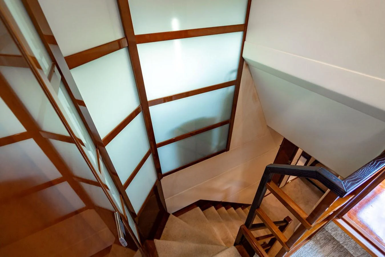 A stylish staircase with wooden accents and frosted glass panels leads to the lower deck. aboard OASIS Yacht for Sale