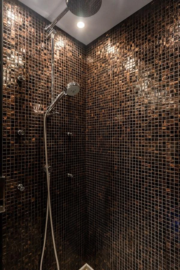 A luxurious shower area with dark mosaic tiles and modern fixtures. aboard OASIS Yacht for Sale