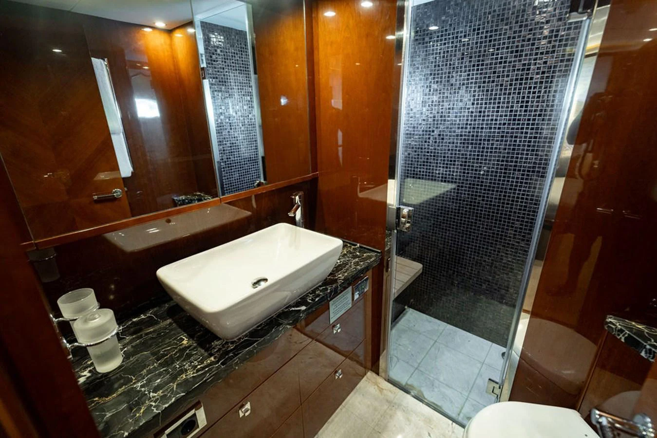 The yacht's bathroom features elegant wood paneling and a modern sink with a sleek black countertop. aboard OASIS Yacht for Sale
