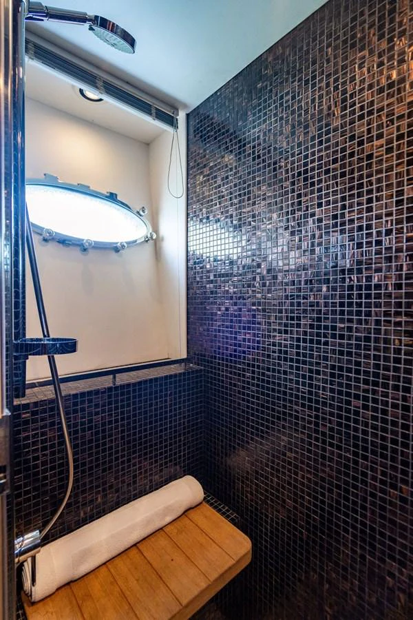A modern yacht shower with dark mosaic tiles and a wooden bench. aboard OASIS Yacht for Sale