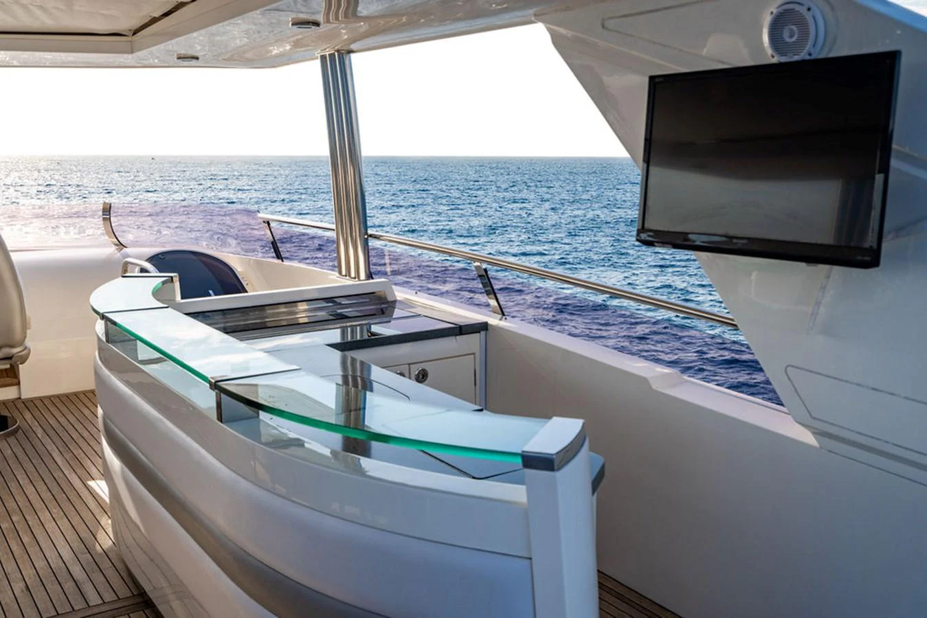 The flybridge features a sleek bar area with a glass countertop and a mounted TV, offering stunning ocean views. aboard OASIS Yacht for Sale