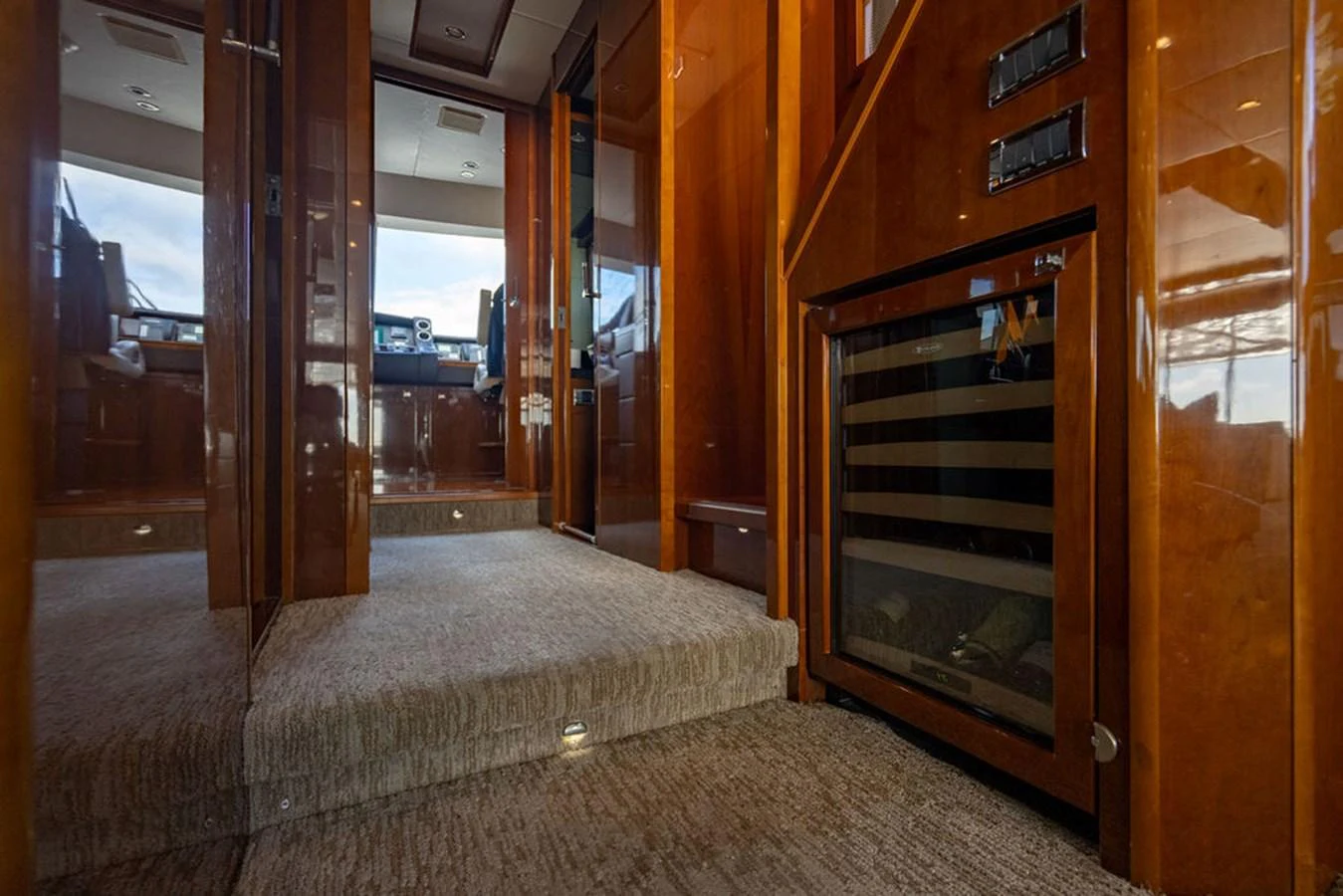 The image showcases a luxurious interior hallway with polished wood finishes and a built-in wine cooler. aboard OASIS Yacht for Sale