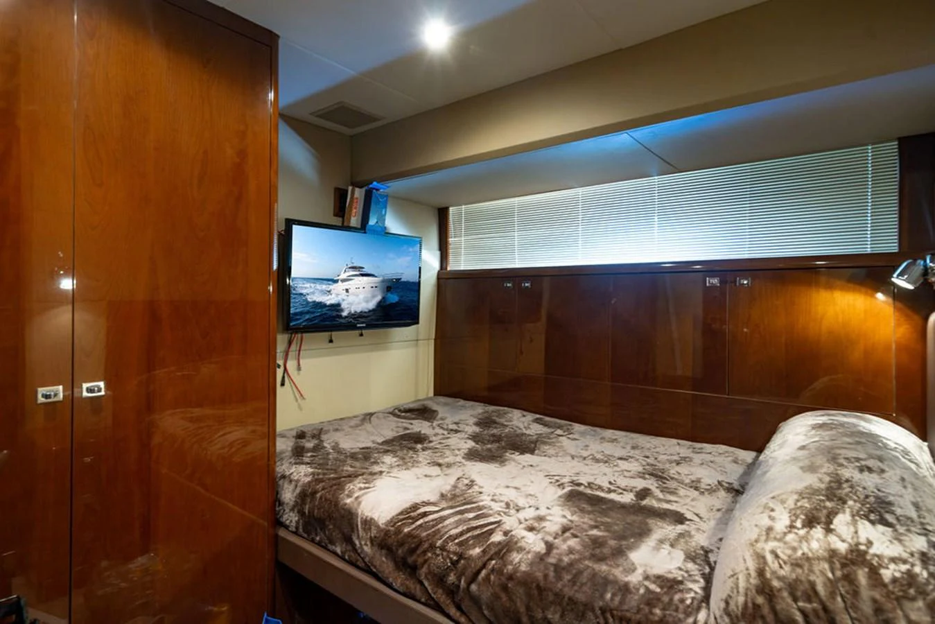 A cozy stateroom with a plush bed and a mounted TV displaying a yacht. aboard OASIS Yacht for Sale