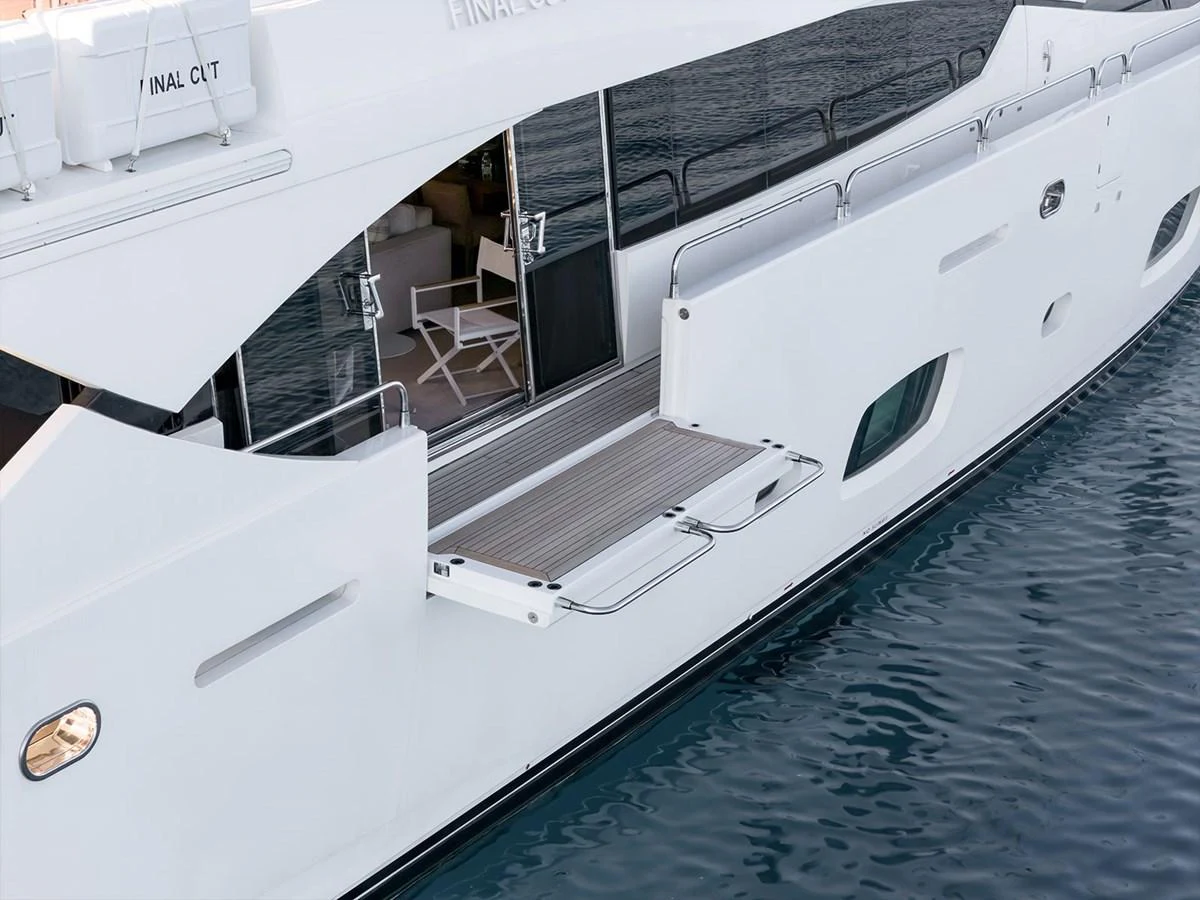 The yacht features a sleek exterior with a fold-out balcony over the water. aboard FINAL CUT Yacht for Sale