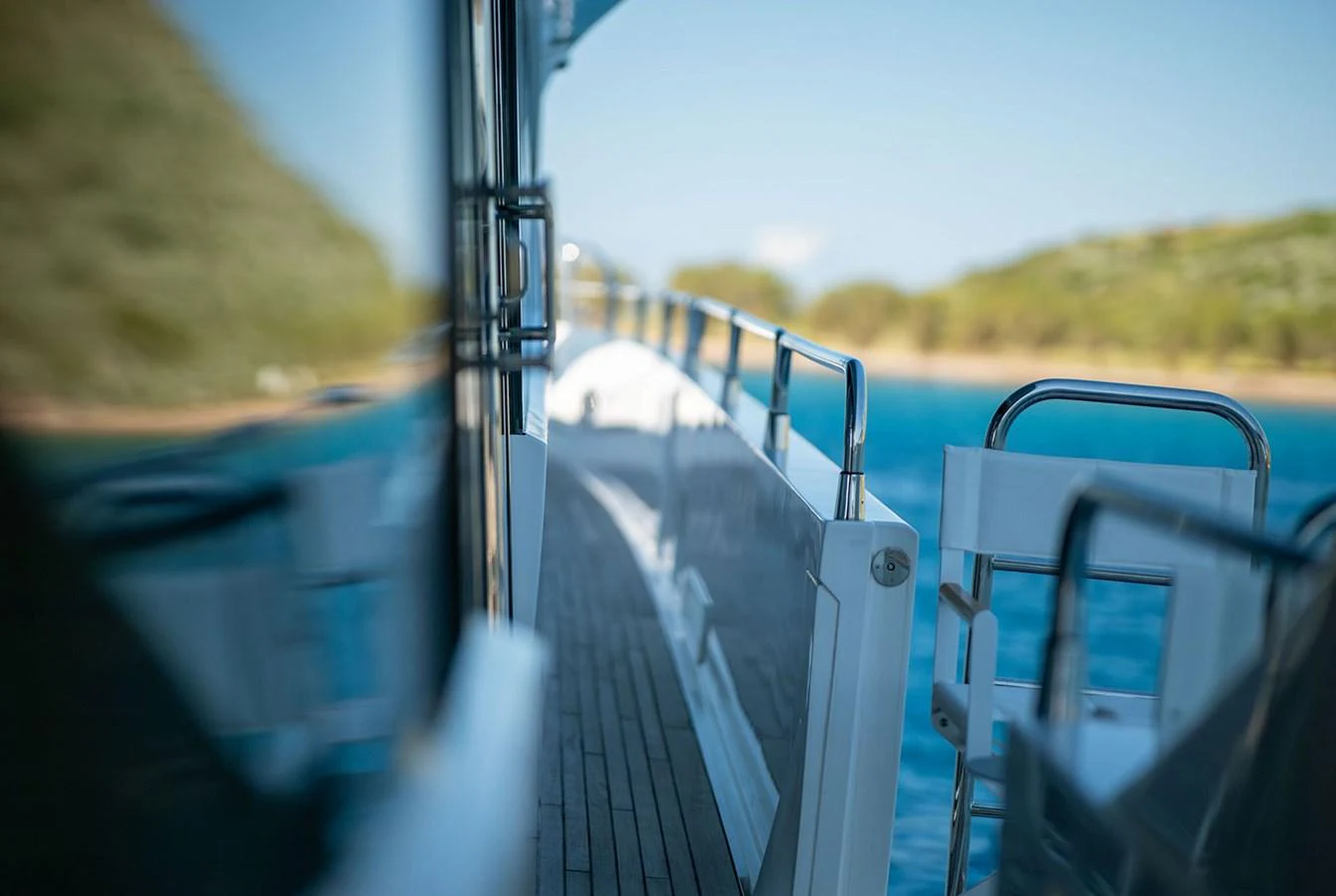 The image captures the sleek side deck of a yacht with a scenic backdrop of water and greenery. aboard FINAL CUT Yacht for Sale