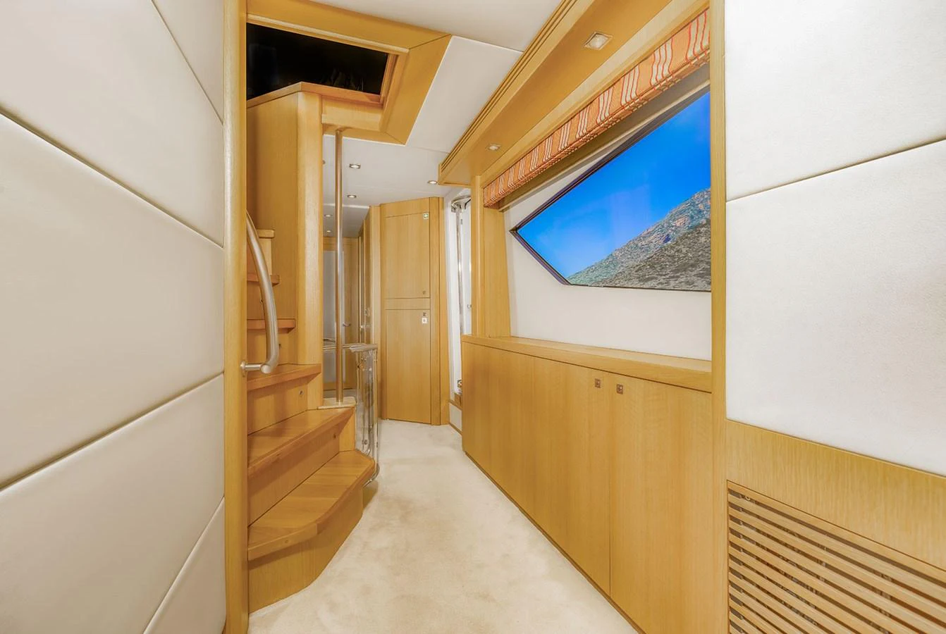 The yacht's interior hallway features elegant wooden finishes and a large window with a scenic view. aboard FINAL CUT Yacht for Sale