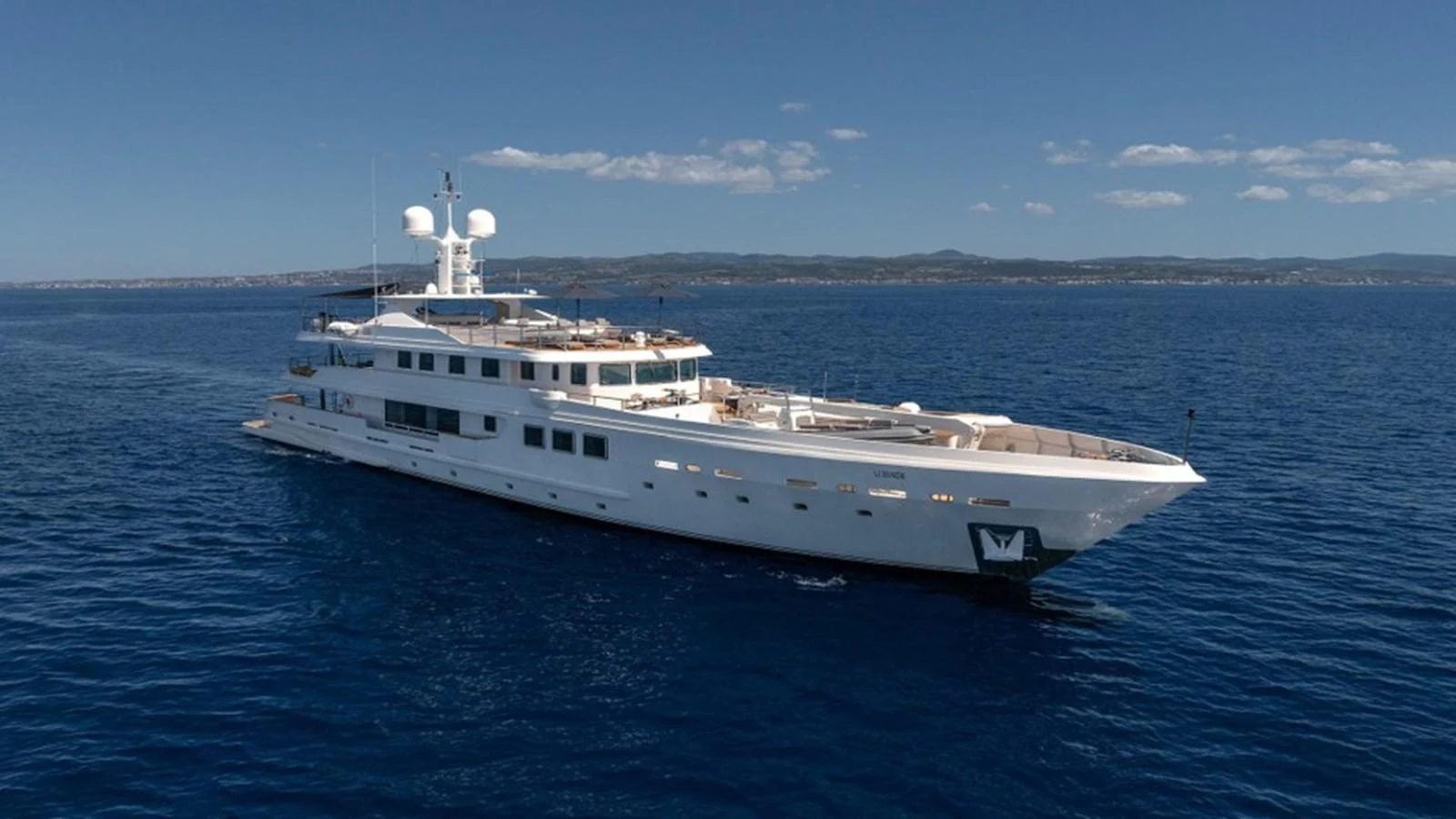 A sleek white yacht cruises through calm blue waters under a clear sky. aboard R23 Yacht for Sale