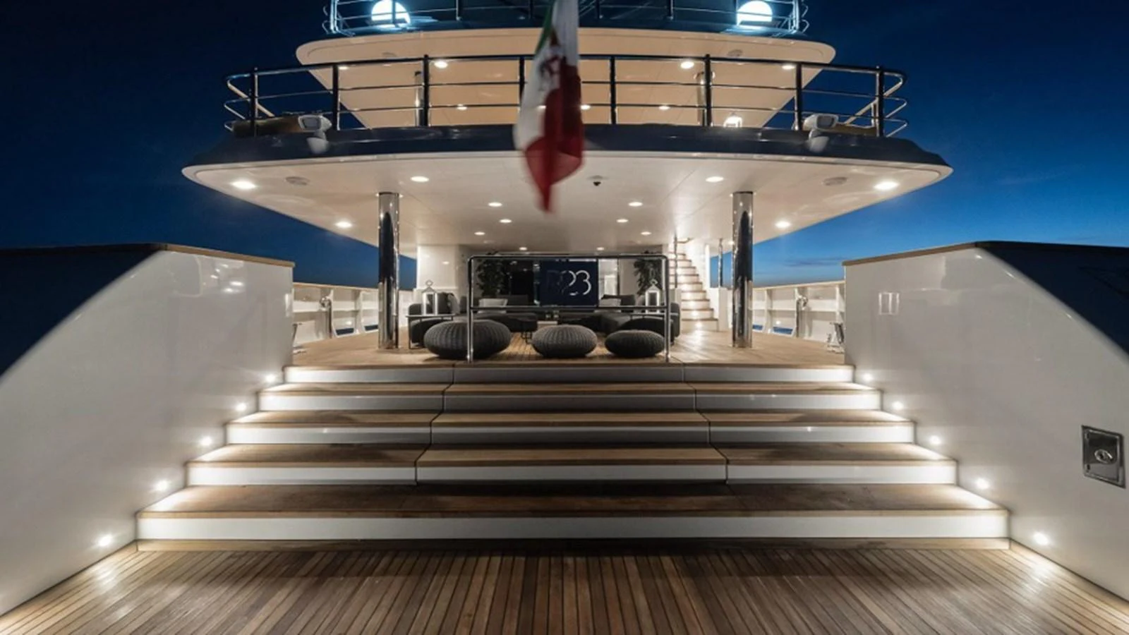 The aft deck of the yacht is beautifully illuminated at night, showcasing elegant steps and a spacious lounging area. aboard R23 Yacht for Sale
