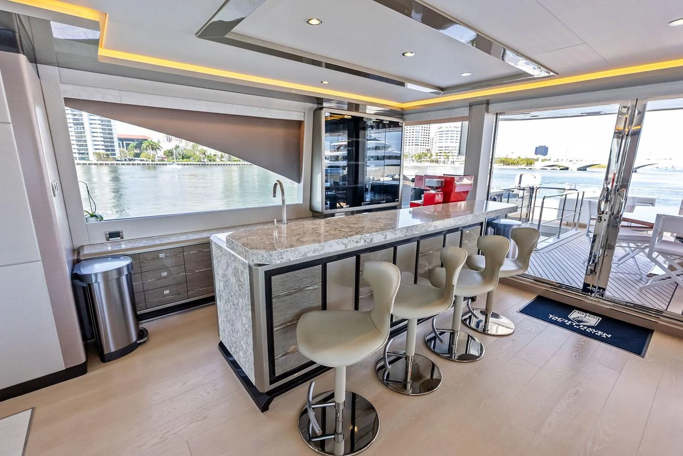The yacht's galley features a sleek bar area with modern stools and a view of the water through large windows. aboard SERENITY NOW Yacht for Sale