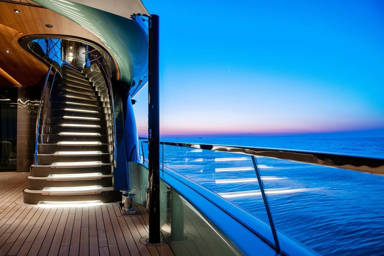 The yacht's deck features a stunning staircase with ambient lighting, set against a serene ocean backdrop at dusk. aboard KENSHO Yacht for Sale