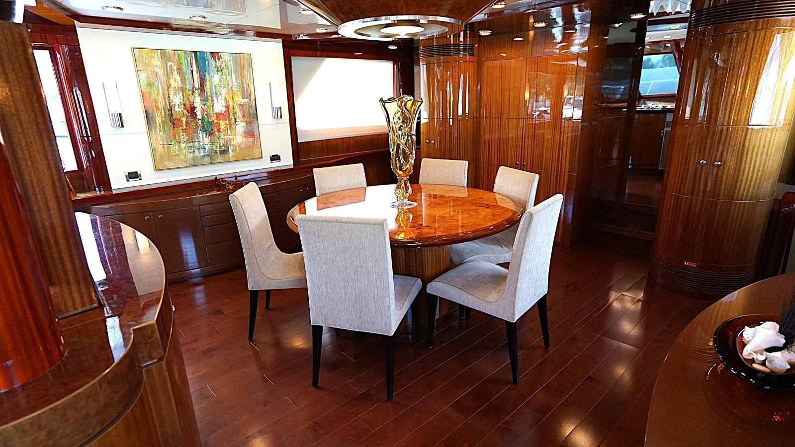 The yacht's dining area features a round wooden table surrounded by upholstered chairs, with elegant wood paneling and contemporary art on the walls. aboard ROBIN'S NEST Yacht for Sale