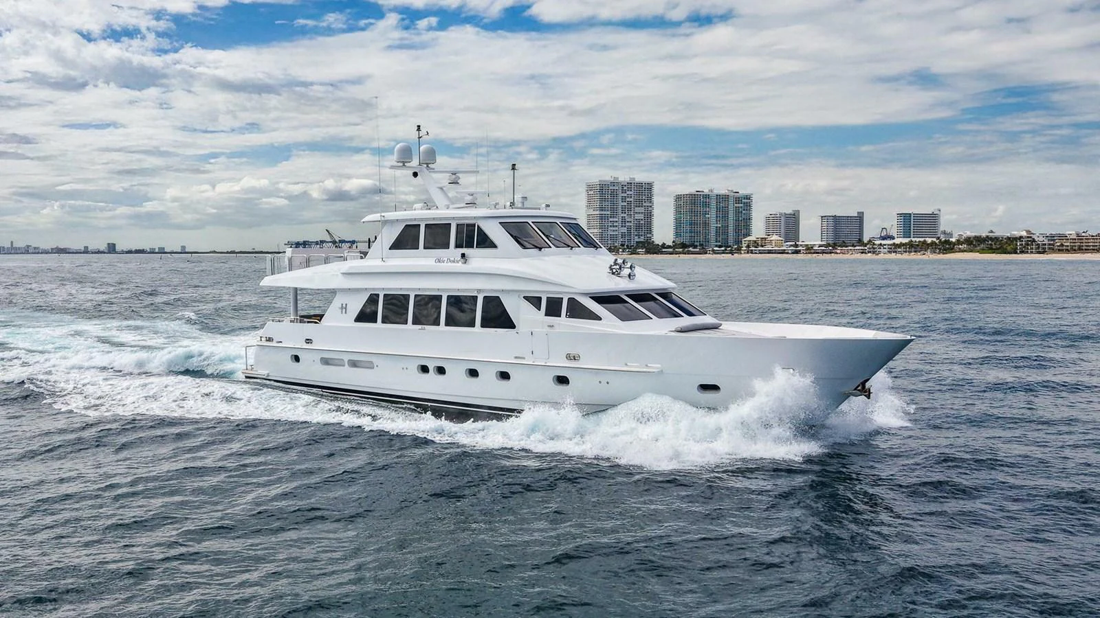 A luxurious yacht cruises through the water with a cityscape in the background. aboard BOBBI TOO Yacht for Sale