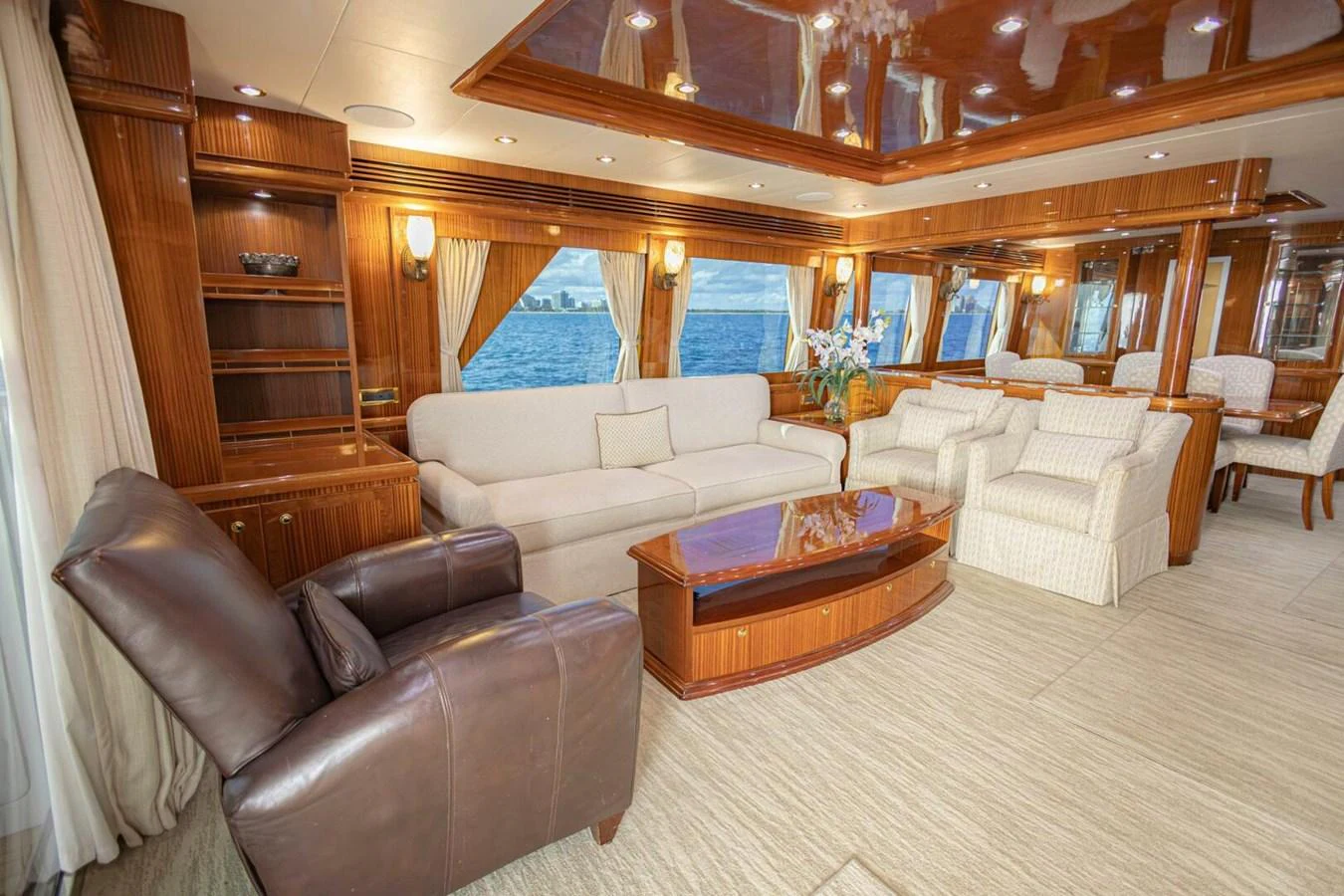 The salon features luxurious seating with elegant wood finishes and panoramic windows offering stunning ocean views. aboard BOBBI TOO Yacht for Sale