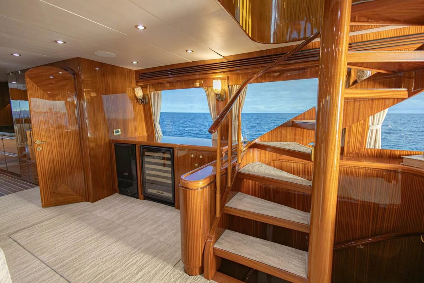 The interior features a beautifully crafted wooden staircase with a view of the ocean through large windows. aboard BOBBI TOO Yacht for Sale