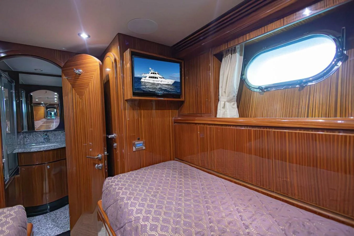 A cozy cabin with a single bed, wooden paneling, and a porthole window. aboard BOBBI TOO Yacht for Sale