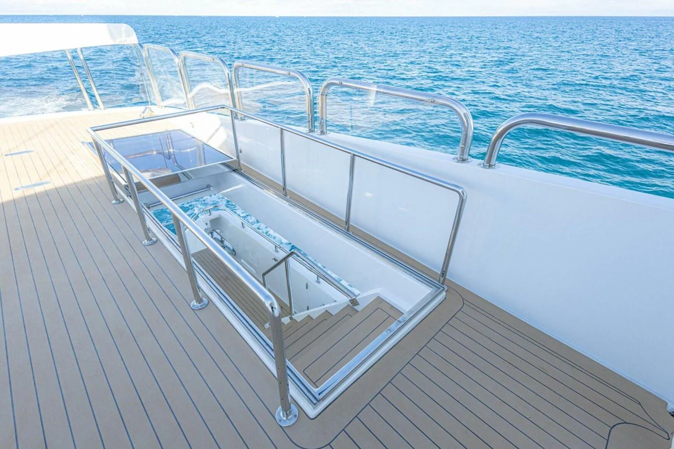 The yacht's deck features a sleek staircase leading down to a lower level, surrounded by clear glass railings and offering stunning ocean views. aboard BOBBI TOO Yacht for Sale