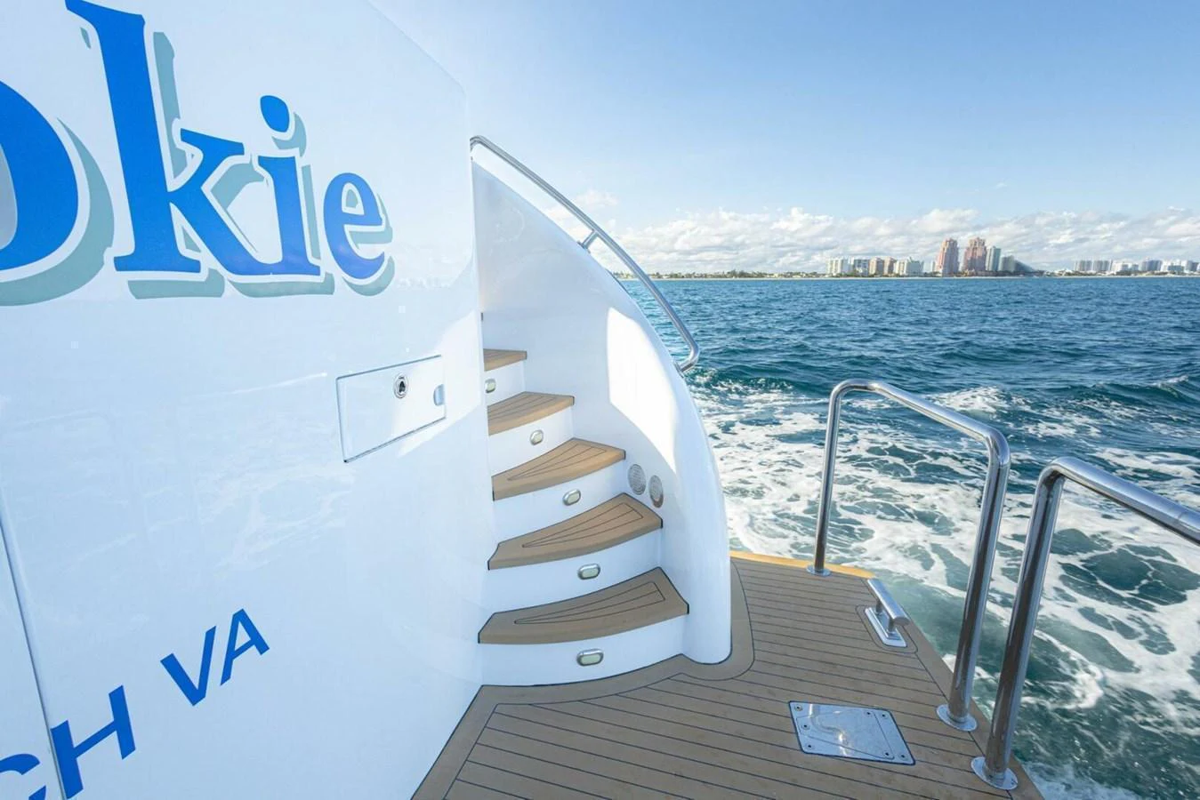 The image showcases the aft deck of a yacht with a staircase leading up, set against a backdrop of calm waters and a distant shoreline. aboard BOBBI TOO Yacht for Sale