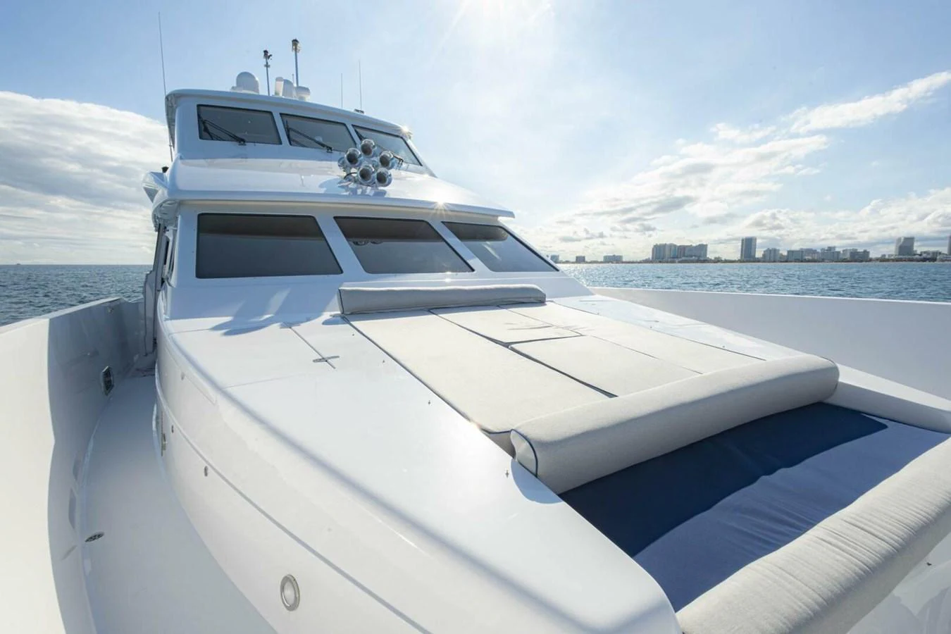 The yacht's foredeck features a spacious sunbathing area with plush cushions, set against a backdrop of calm waters and a clear sky. aboard BOBBI TOO Yacht for Sale