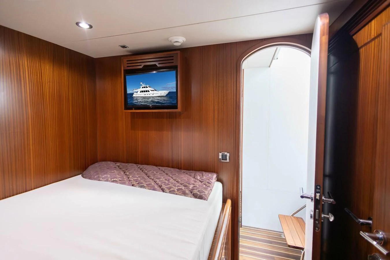 A cozy guest cabin with a comfortable bed and a wall-mounted TV displaying a yacht. aboard BOBBI TOO Yacht for Sale
