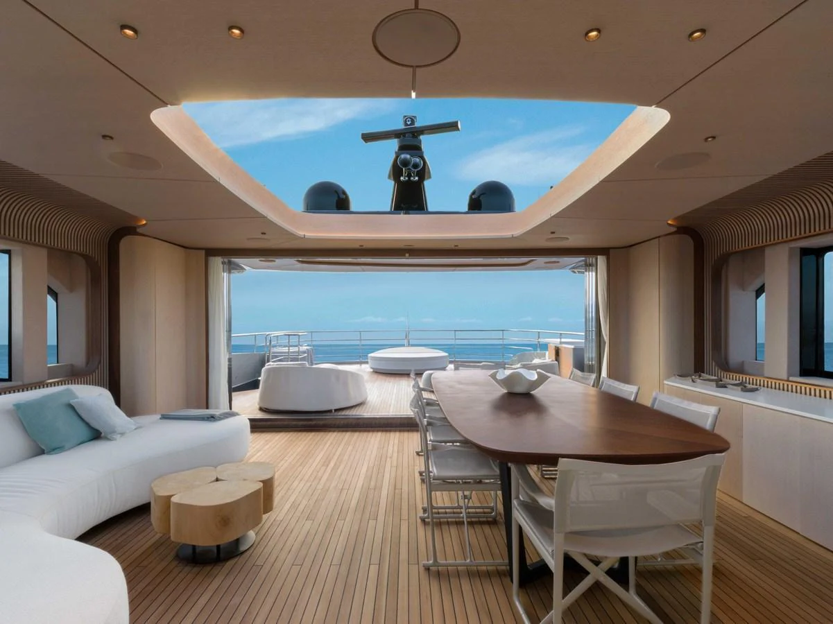 This elegant salon features a spacious seating area and a dining table with a stunning view of the ocean through large windows and an open ceiling. aboard PESA II Yacht for Sale