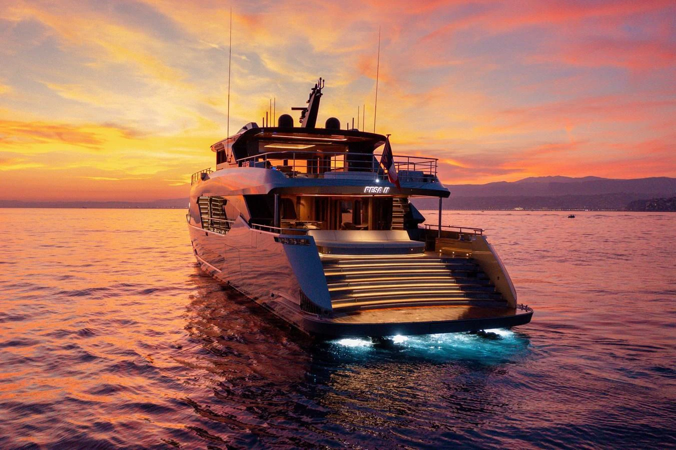 A sleek yacht is beautifully illuminated against a stunning sunset backdrop on the open water. aboard PESA II Yacht for Sale