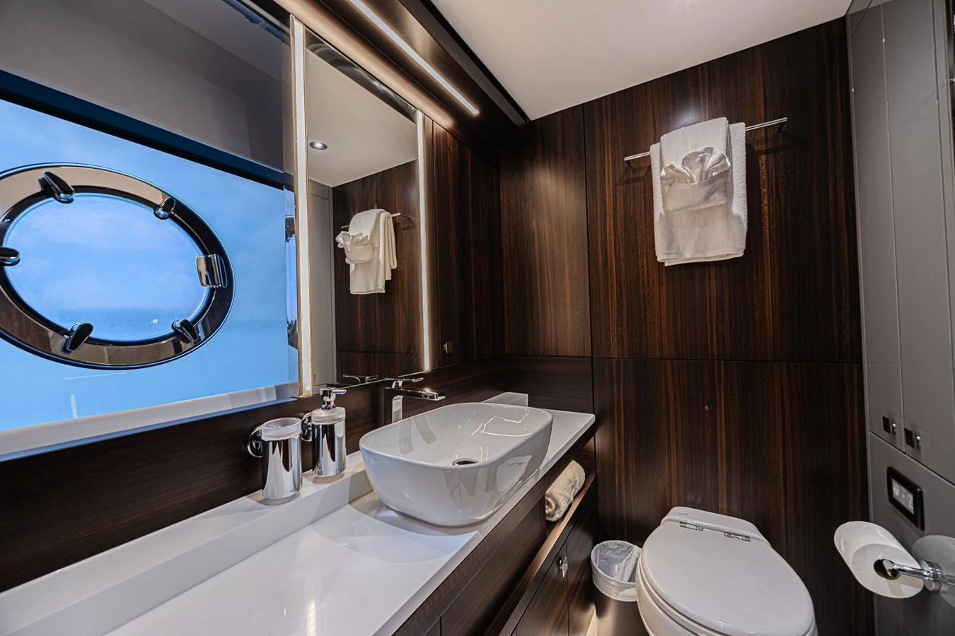 The yacht's bathroom features sleek modern design with dark wood accents and a porthole window. aboard HIDEOUT Yacht for Sale