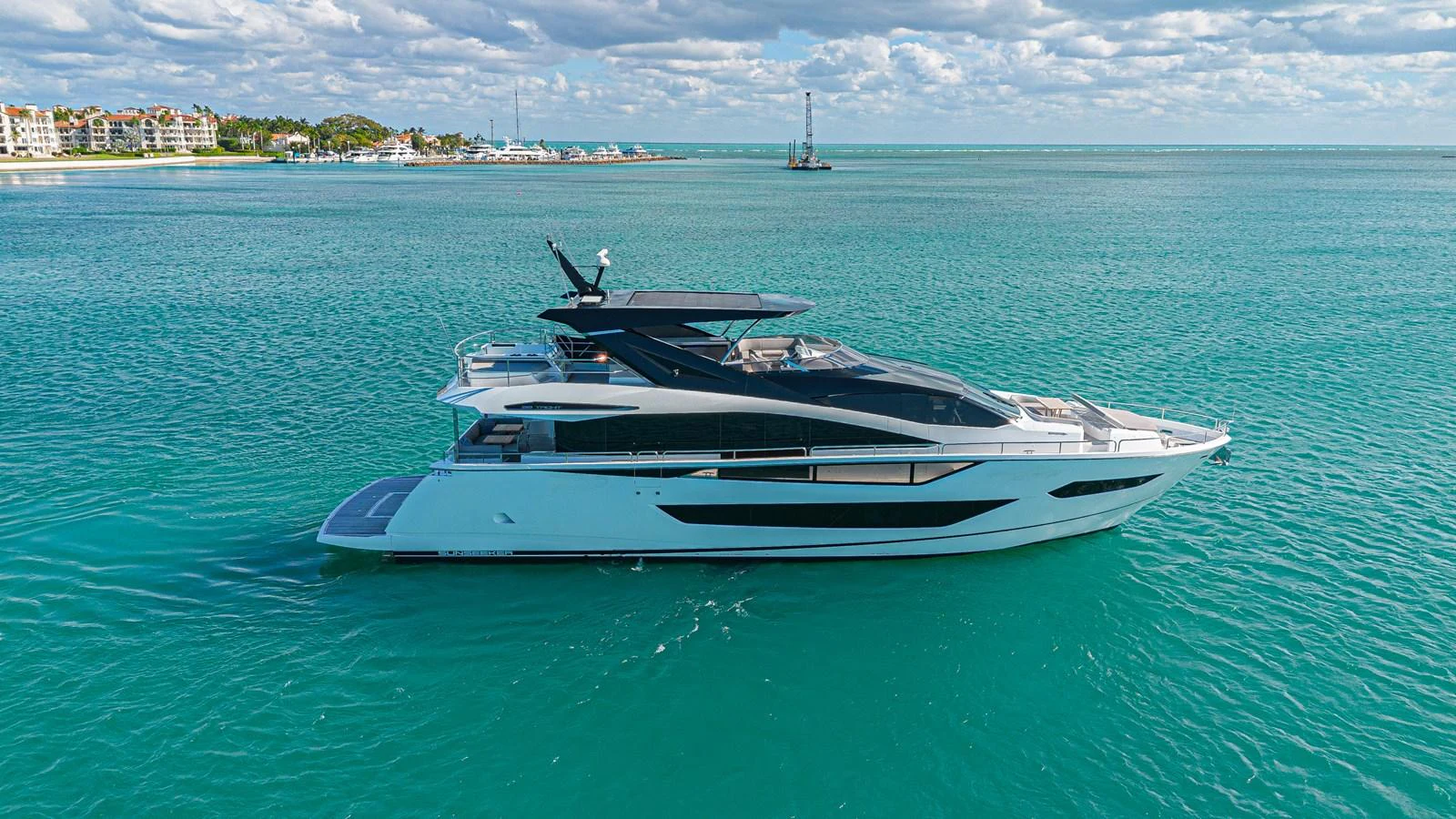 A sleek, modern yacht glides gracefully on turquoise waters under a partly cloudy sky. aboard HIDEOUT Yacht for Sale