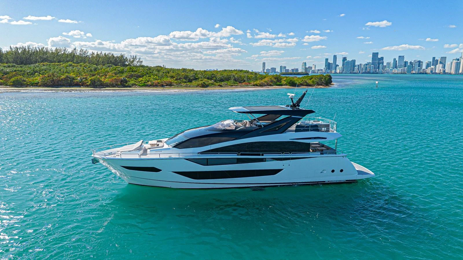 A sleek and modern yacht cruises along a serene coastline with a city skyline in the background. aboard HIDEOUT Yacht for Sale