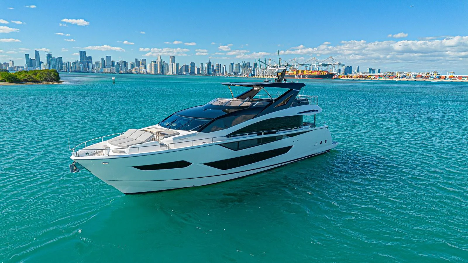 A sleek and modern yacht cruising on clear blue waters with a city skyline in the background. aboard HIDEOUT Yacht for Sale