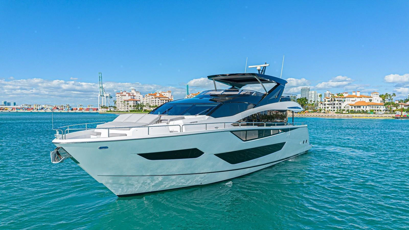 A sleek and modern yacht cruising on calm waters with a cityscape in the background. aboard HIDEOUT Yacht for Sale