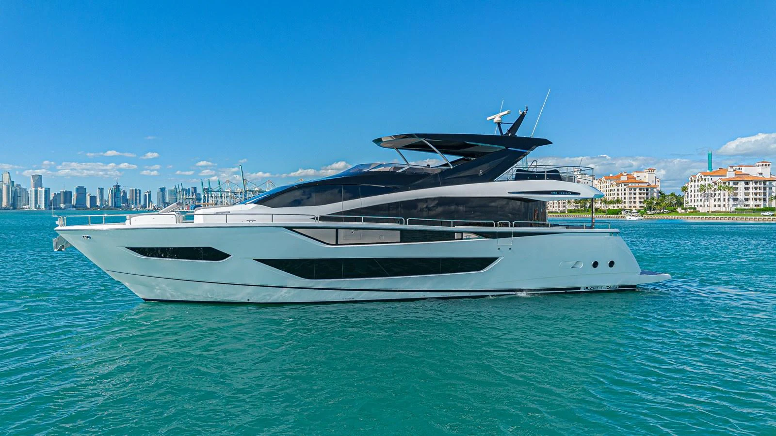 A sleek and modern yacht cruising on calm waters with a cityscape in the background. aboard HIDEOUT Yacht for Sale