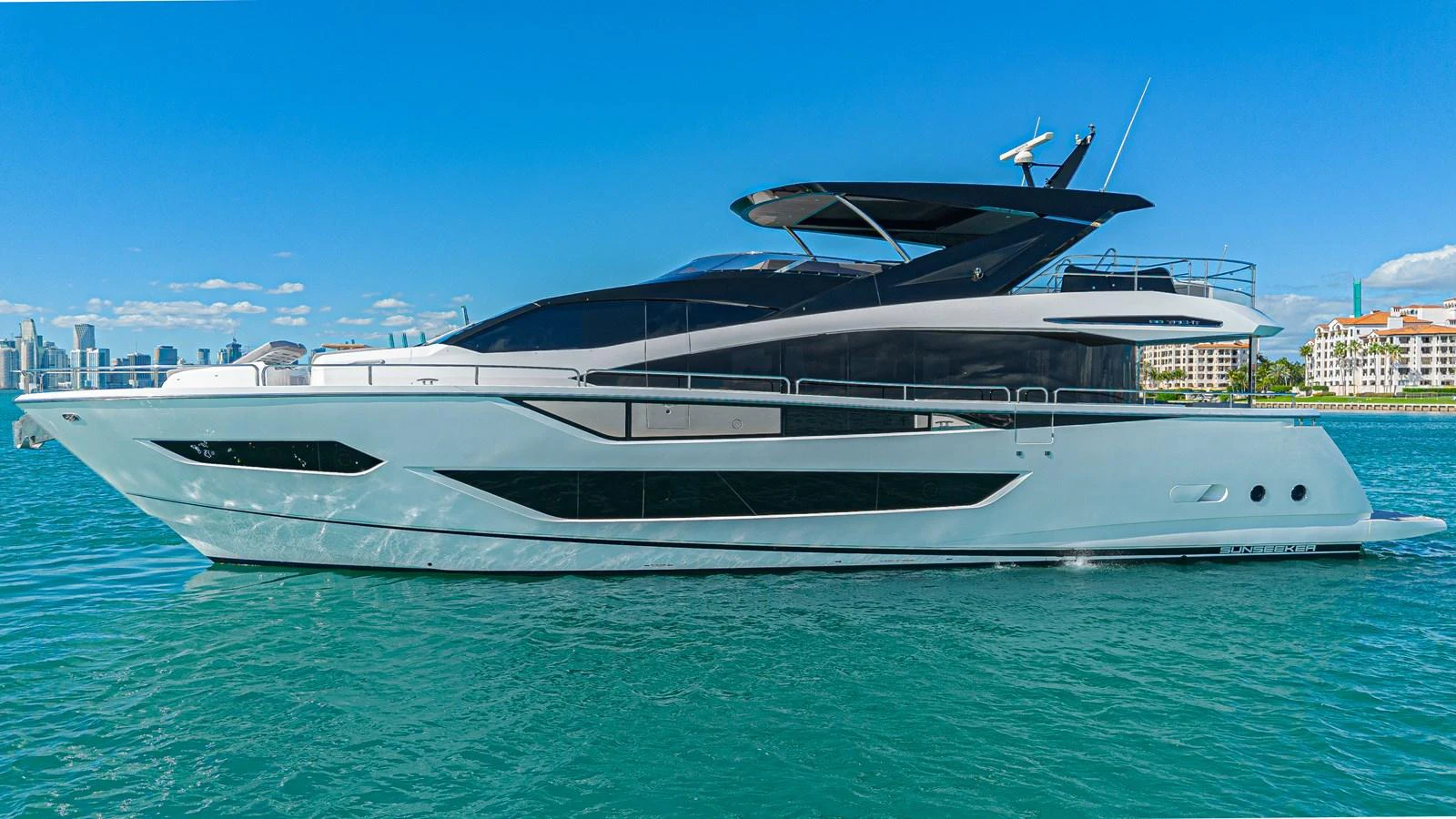 A sleek and modern yacht cruising on calm waters with a cityscape in the background. aboard HIDEOUT Yacht for Sale