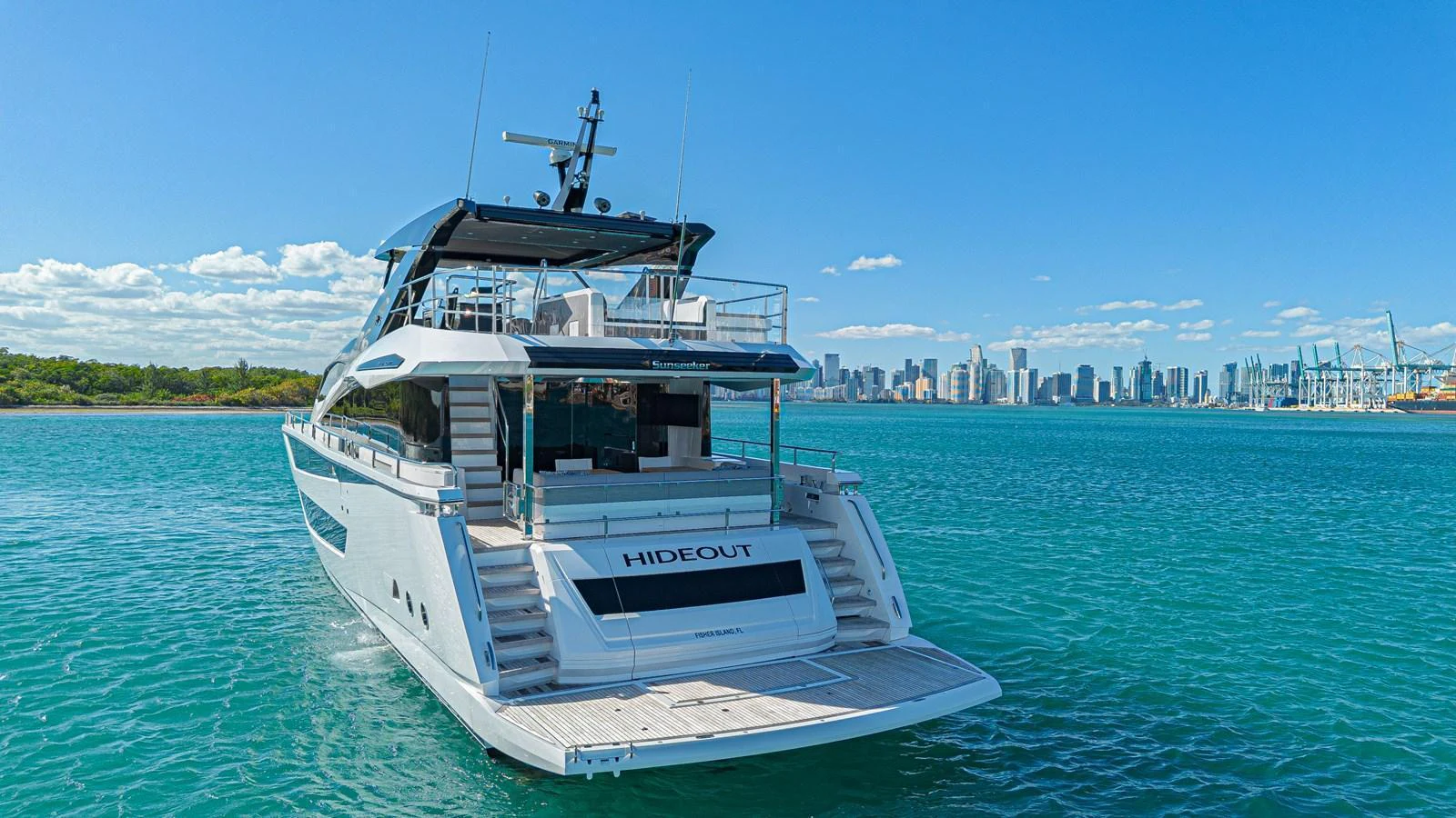A sleek yacht is anchored in calm waters with a city skyline in the background. aboard HIDEOUT Yacht for Sale