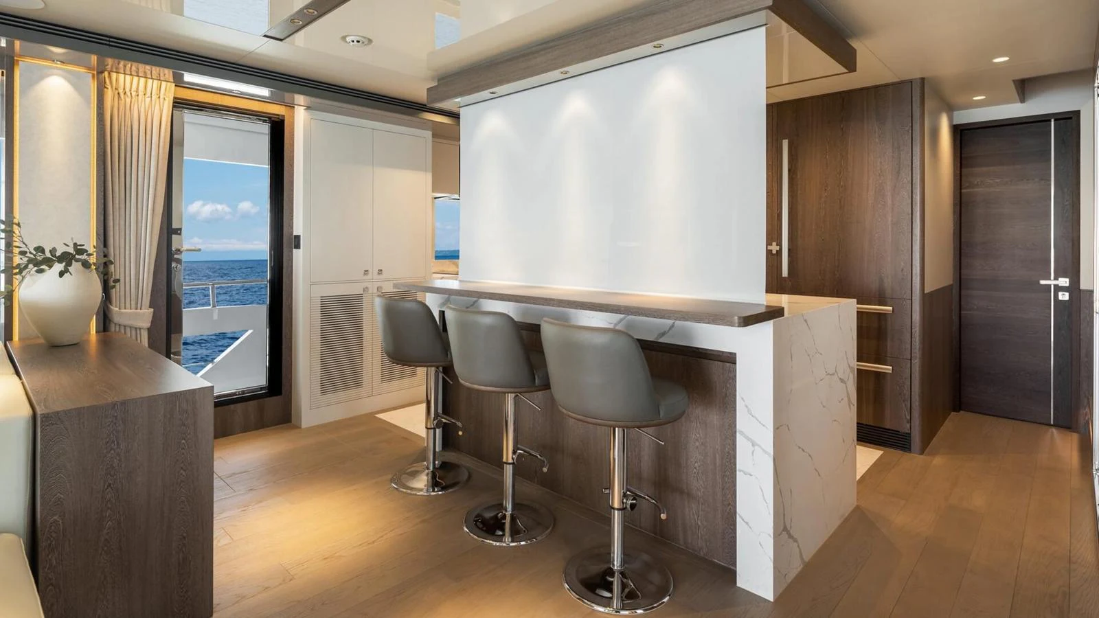 The galley features modern bar seating and sleek cabinetry with a view of the ocean through the open door. aboard HAPPY HEART Yacht for Sale