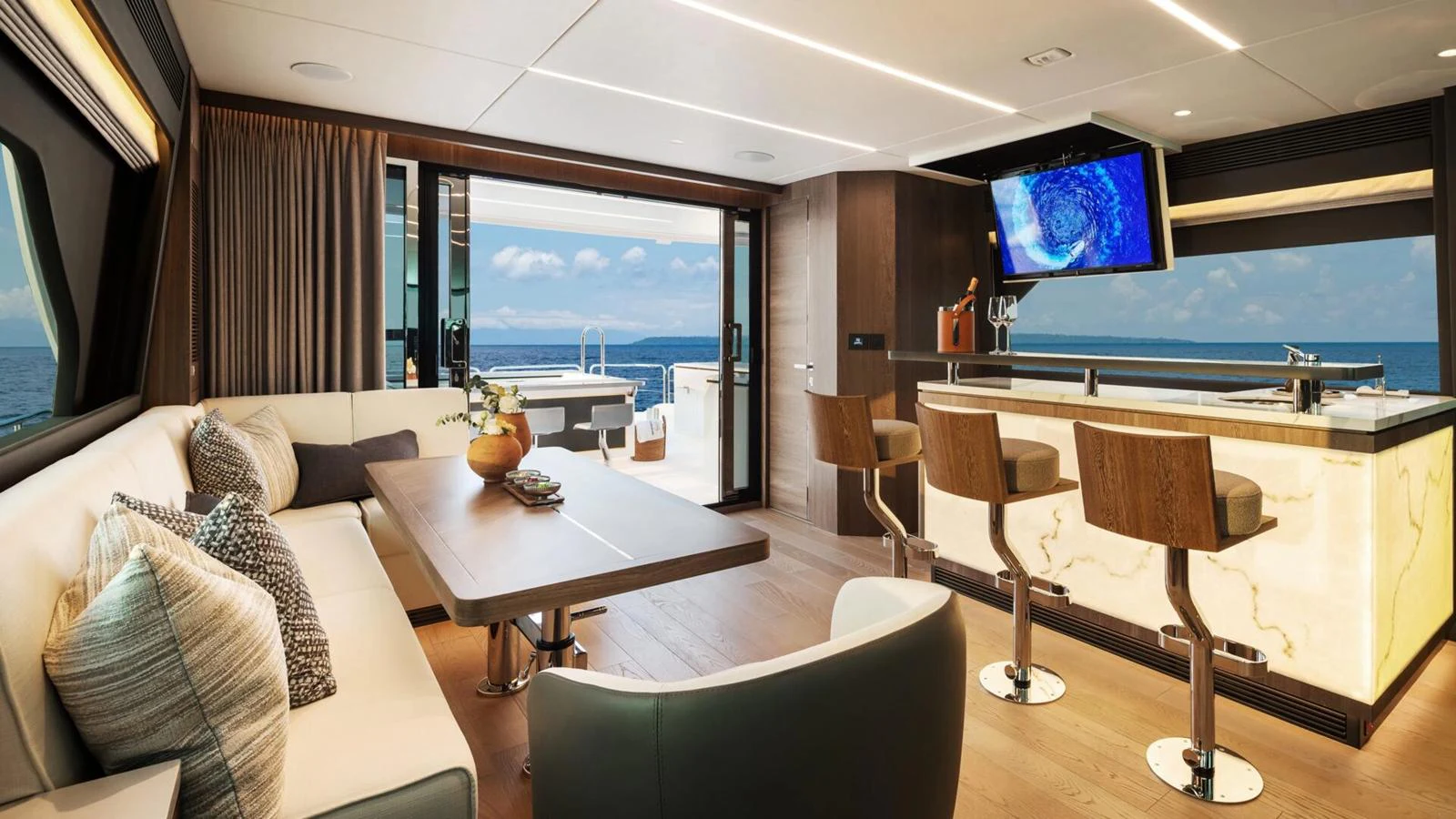 The salon offers a luxurious and inviting space with a comfortable seating area, a stylish bar, and a large TV, all with a stunning view of the ocean. aboard HAPPY HEART Yacht for Sale