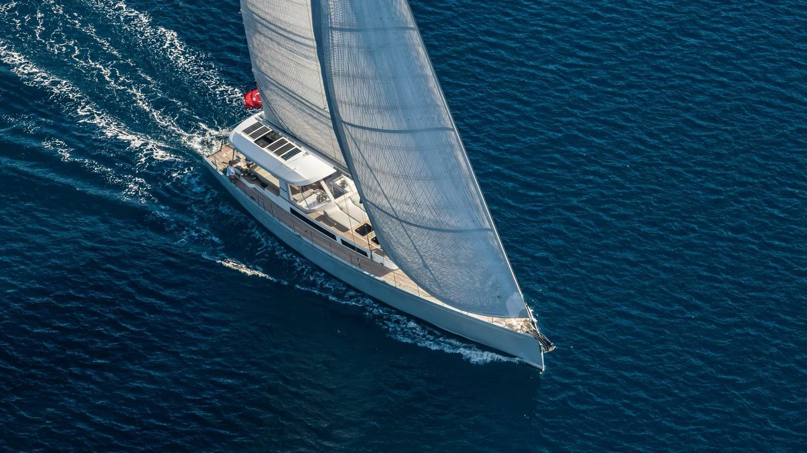 A sleek sailing yacht glides gracefully over the deep blue sea, showcasing its elegant design and impressive sail. aboard MISHI Yacht for Sale