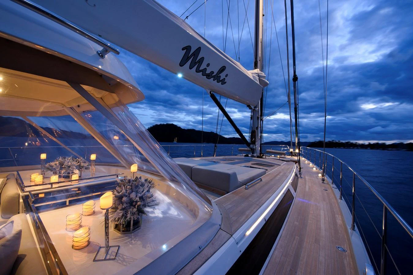 The yacht's deck is beautifully illuminated at dusk, showcasing elegant outdoor dining and lounging areas. aboard MISHI Yacht for Sale