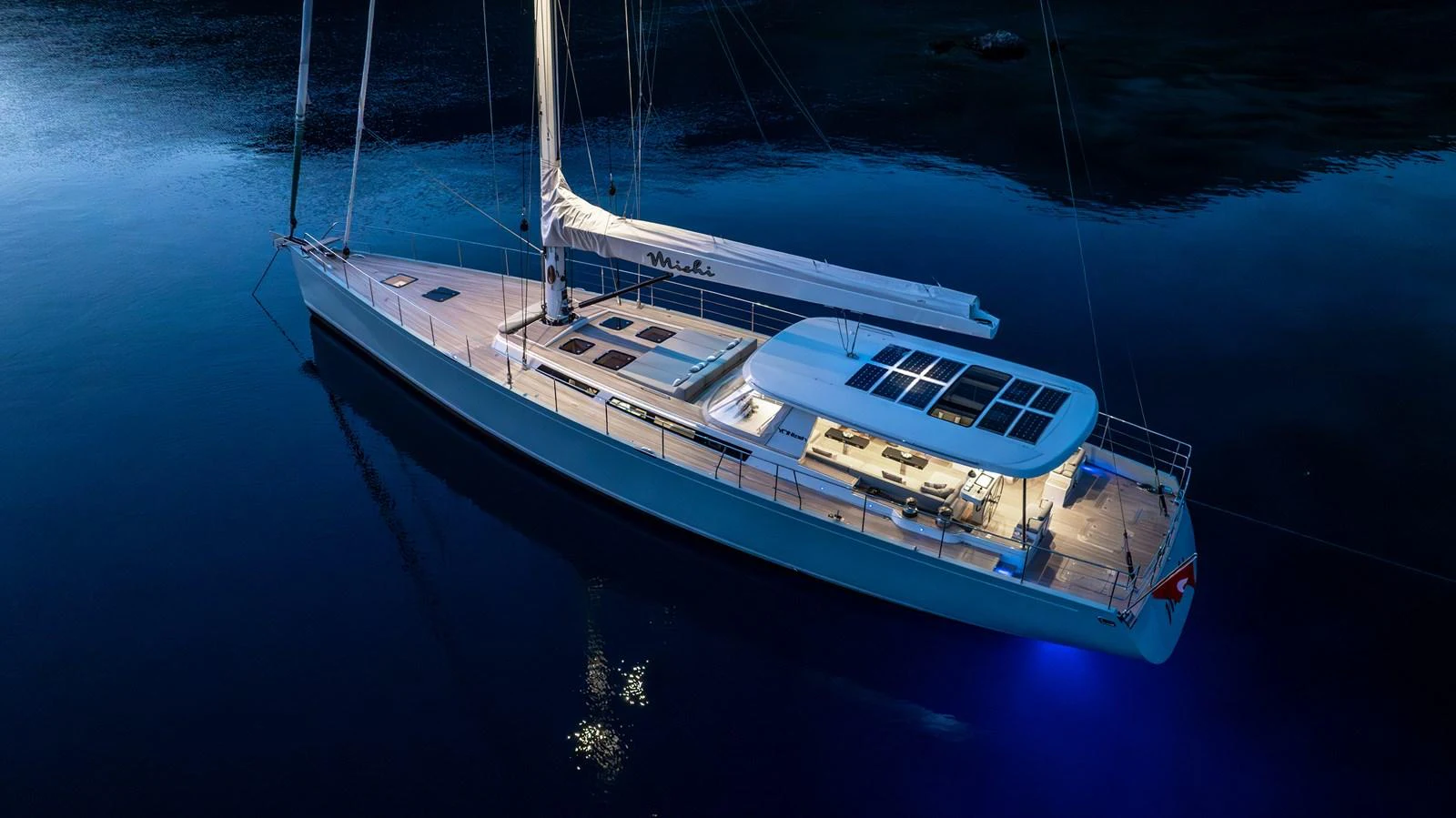 A sleek and modern sailing yacht is illuminated against the tranquil evening waters. aboard MISHI Yacht for Sale