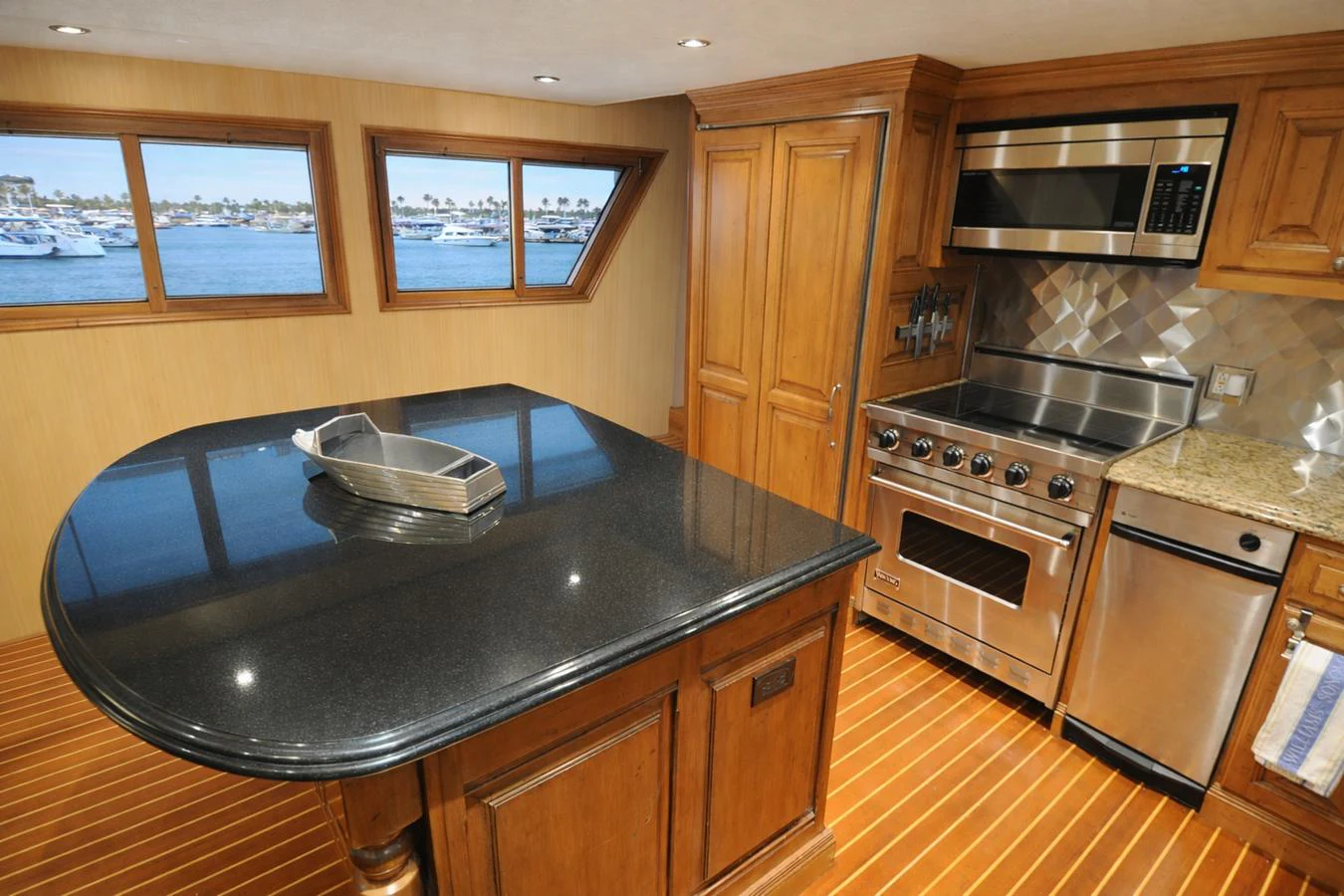 The galley features modern stainless steel appliances and elegant wood cabinetry, with a view of the marina through large windows. aboard BURNING DAYLIGHT Yacht for Sale