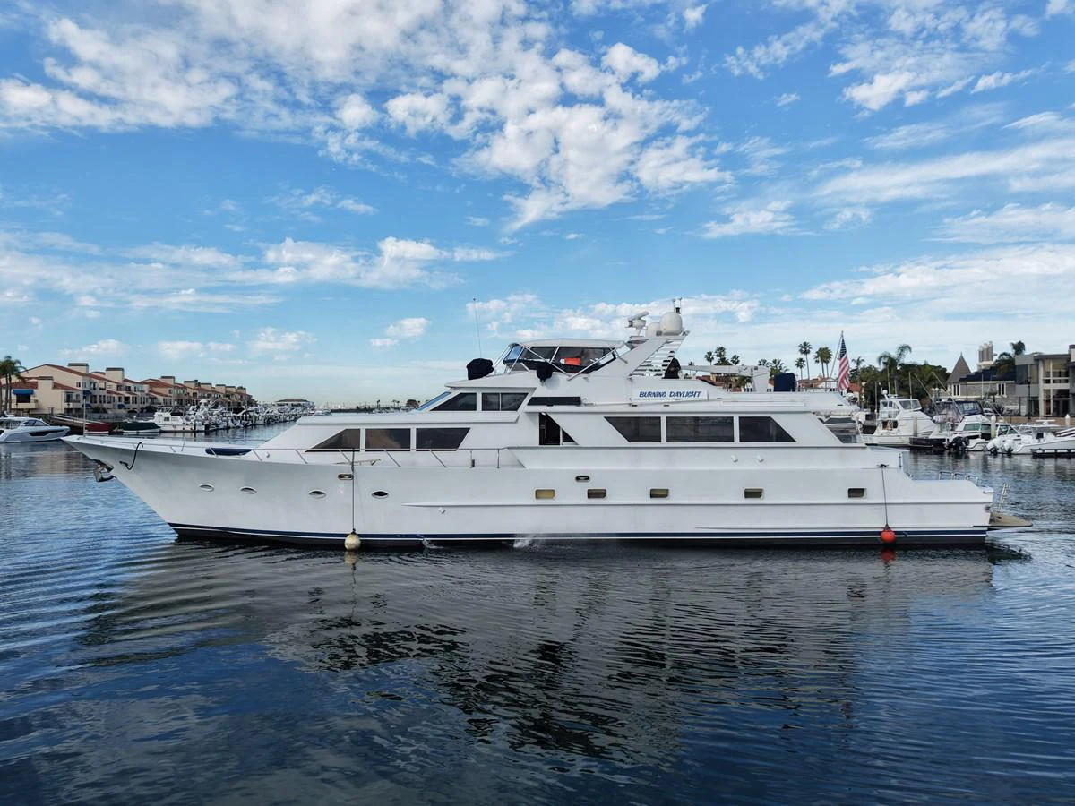 A sleek white yacht is docked in a calm marina under a partly cloudy sky. aboard BURNING DAYLIGHT Yacht for Sale