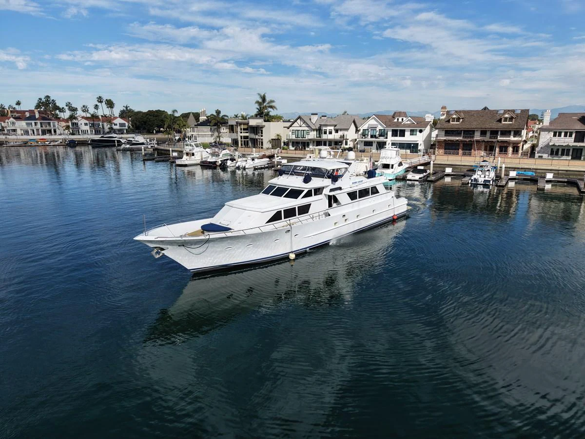 A sleek white yacht is docked in a serene marina with charming waterfront homes in the background. aboard BURNING DAYLIGHT Yacht for Sale