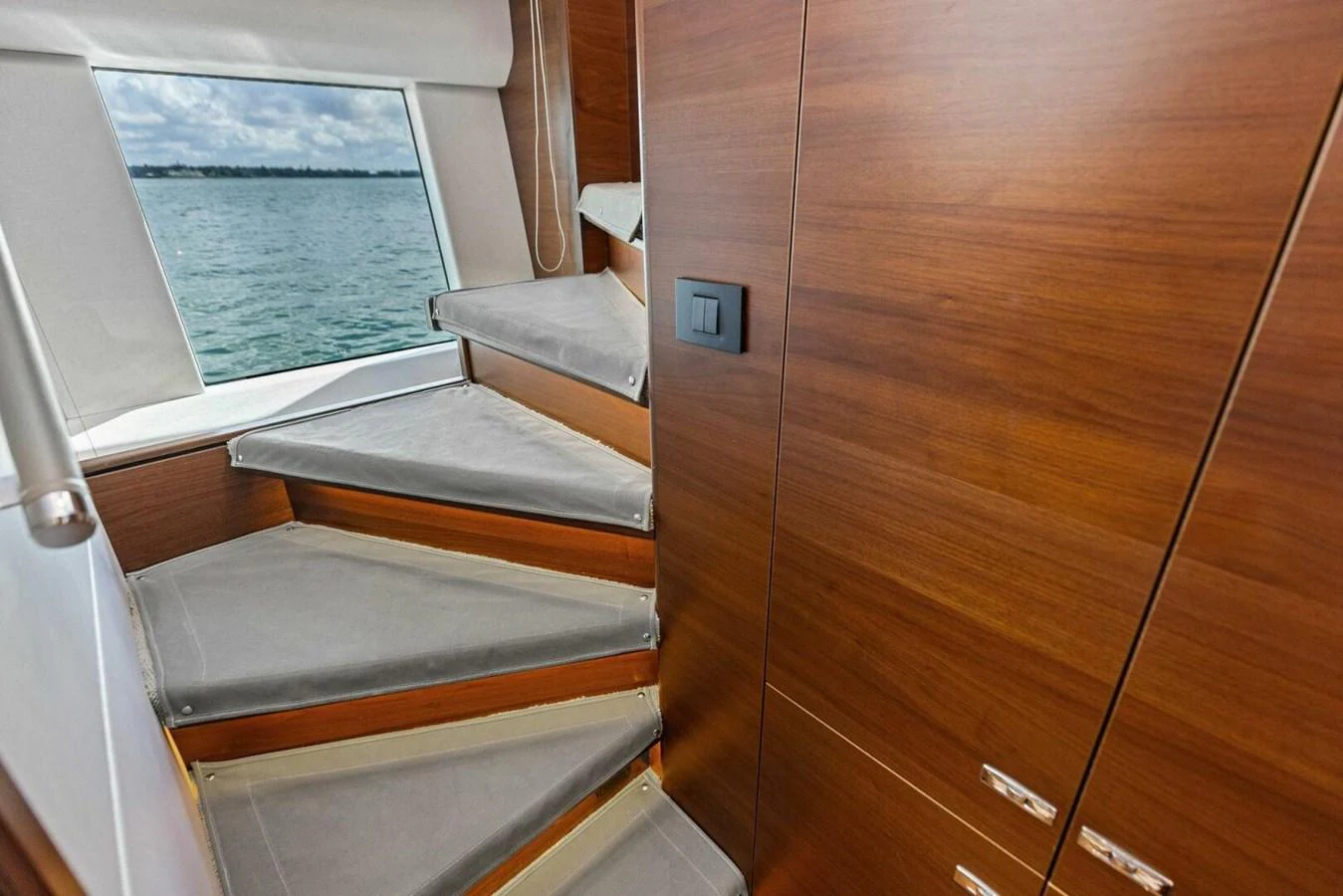 A modern yacht interior featuring a sleek wooden staircase with a view of the sea through a window. aboard 3BBOYS Yacht for Sale