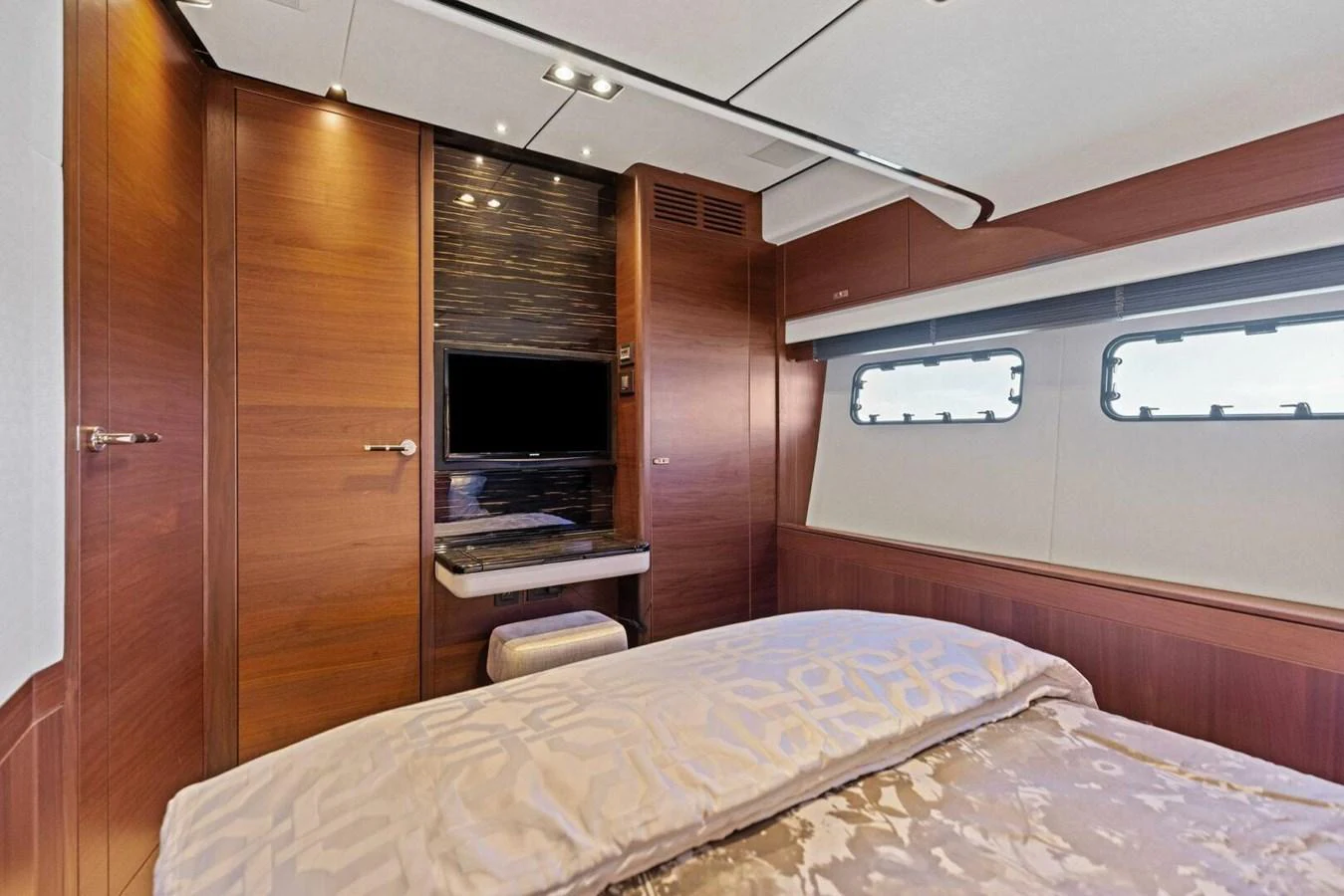 A luxurious stateroom featuring a comfortable bed, wood paneling, and a mounted television. aboard 3BBOYS Yacht for Sale