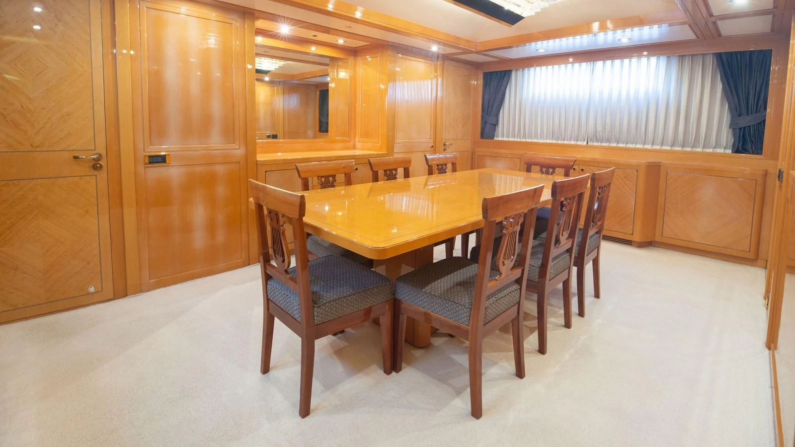 The yacht's dining area features a polished wooden table surrounded by elegant chairs, set within a warmly lit space. aboard BLUE RIBBON Yacht for Sale