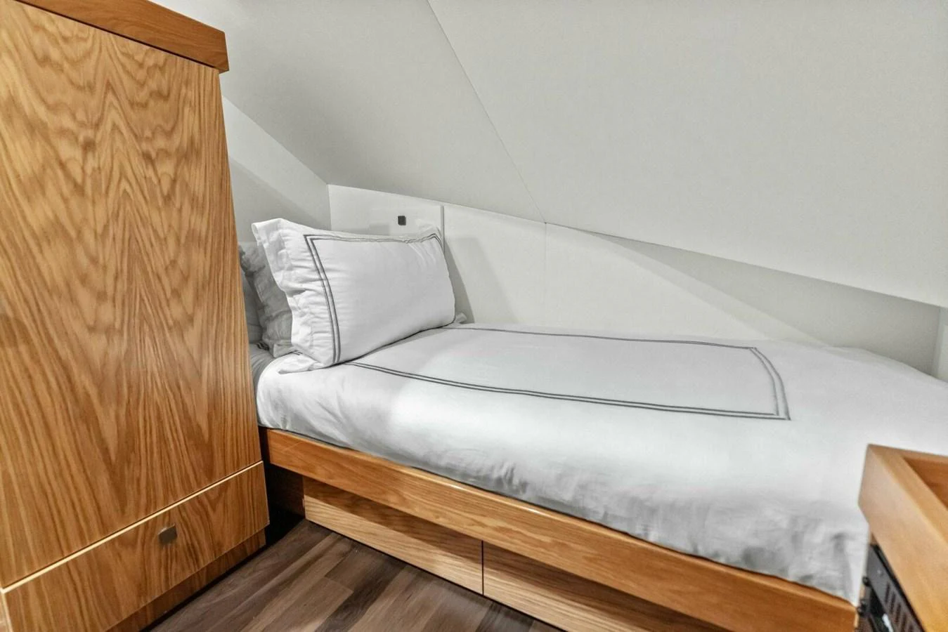 A cozy guest cabin featuring a single bed with crisp white linens and wooden cabinetry. aboard TEAM HARVEY I Yacht for Sale