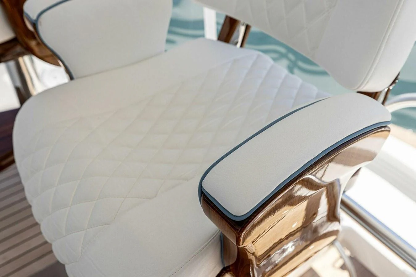 A close-up of a luxurious, quilted white seat with wooden armrests on a yacht. aboard TEAM HARVEY I Yacht for Sale